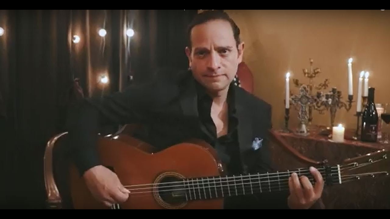 David Maldonado in formal black attire playing flamenco guitar by candlelight with fairy lights behind him