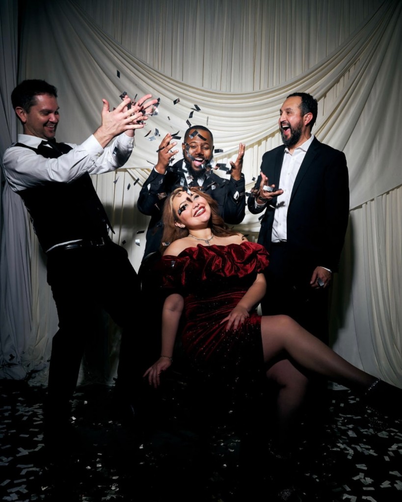 Stephanie Salahz in a burgundy velvet gown with three formally dressed bandmates as silver confetti falls