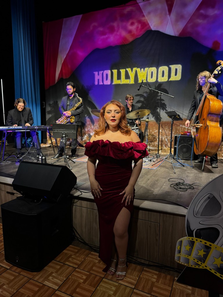 Stephanie Salahz in a red velvet gown center stage with keyboard, sax, drums, and upright bass, Hollywood sign backdrop
